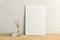 Blank vertical poster frame mock up standing on light herringbone parquet floor next to white brick wall with vase and books