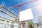 Blank white billboard in front of construction site with scaffolding and crane