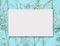 Blank white greeting card layout on little white flowers at turquoise blue