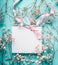 Blank white greeting card with pink ribbon on little white flowers at turquoise blue background