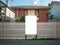 Blank white mock up template of a real estate advertisement billboard/sign/board at front of a typical residential brick house