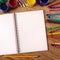 Blank white open notebook on a school desk with various paints, pencils and crayons