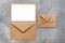 Blank white paper card mockup, brown craft envelope and letter. Gray concrete grunge background. Modern stationery still life. Top