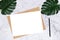 Blank white paper size A4 on brown paper envelope on white marble background with green palm leaf on desk for decoration.