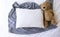 Blank white rectangle cushion laying on a grey scarf with a white duvet background and child`s teddy