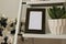 Blank wooden photo frame surrounded by home plants. Comfy details in the bedroom