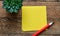 Blank yellow memo card and yellow pencil on a wooden table. A blank space to enter a note or insert graphics