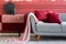 Blanket and burgundy pillows on grey sofa in trendy living room interior with chest of drawers