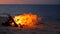 Blazing campfire on beach, summer evening. Bonfire in nature as background. Burning wood on white sand shore at sunset.