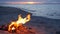 Blazing campfire on beach, summer evening. Bonfire in nature as background. Burning wood on white sand shore at sunset.