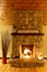 A blazing fire in a large stone fireplace with a farmhouse sign, reeds, logs and candles.