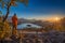 Bled, Slovenia - Photographer traveler wearing orange jacket and hat taking photos of the panoramic autumn sunrise