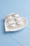 Blister pack of medical pills in a white plate in the shape of a heart on a wooden blue