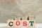 Block in word cost with coin in up trend on wood background