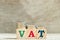 Block in word VAT Value added tax with coin in down trend on wood background