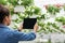 Blog for work. African american girl holding tablet with empty screen, making photo of flowers in pots hanging from the