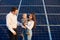 Blond baby in arms of mom near dad looks into the distance against background solar panels.