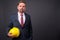 Blond bearded businessman with goatee holding hardhat against gr