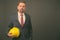 Blond bearded businessman with goatee holding hardhat against gray background