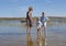 Blond beautiful mother with her two kids, standing in a lake with aquatic plants and a boat, in the background a green landscape