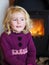 Blond blue eyed little girl sitting in front of a fireplace