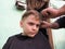 A blond boy of 8 years old gets his hair cut with scissors. Hairdresser services at home. Haircut for a child with blond