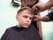 A blond boy of 8 years old gets his hair cut with scissors. Hairdresser services at home. Haircut for a child with blond hair