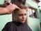 A blond boy of 8 years old gets his hair cut with scissors. Hairdresser services at home. Haircut for a child with blond hair