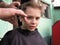 A blond boy of 8 years old gets his hair cut with scissors. Hairdresser services at home. Haircut for a child with blond hair