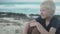 A blond boy sits on the beach by the ocean