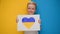 Blond boy smiles holding banner with yellow-blue heart drawn with marker in rivers. Kid will support Ukraine by showing