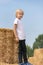 Blond boy standing on haystack in field. Full-length portrait of child near the sheaf of hay in the village