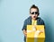 Blond boy in stylish casual clothing and sunglasses holding big yellow present box