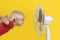 Blond boy with ventilator relaxing on yellow background. Summer heat