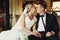 Blond bride kisses a groom sitting with him on a sofa in a hall