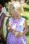 Blond caucasian baby girl peels an orange. Child in white and pink dress holds in hands juicy citrus. Summer day harvest