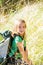 Blond explorer kid girl walking with backpack in grass