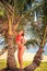 blond girl in bikini stands between palms holds branch