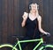 blond girl in black binding outfit and sneakers posing against a wooden background next to a bright bike fixed