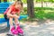 A blond girl dresses red rollers, sitting in a park on a blue bench.