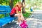 A blond girl dresses red rollers, sitting in a park on a blue bench.