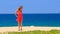 blond girl in red dances barefoot on sand holds hands on hips