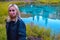 Blond girl is standing and looking at the camera on the background of a picturesque turquoise geyser lake,in which