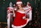 Blond girl wears Santa costume,posing beside Christmas tree and chimney