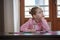 Blond hair school girl boring and tired looking up, sitting at the desk with school supplies, holding her hand over the cheek