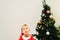 Blond and handsome 5 year old boy dressed as Santa Claus bored by the Christmas tree while waiting for the arrival of the real