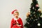 Blond and handsome 5 year old boy dressed as Santa Claus bored by the Christmas tree while waiting for the arrival of the real