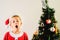 Blond and handsome 5 year old boy dressed as Santa Claus bored by the Christmas tree while waiting for the arrival of the real