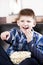 Blond happy boy watching tv and eating popcorn