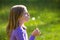 Blond kid girl blowing dandelion flower in green meadow